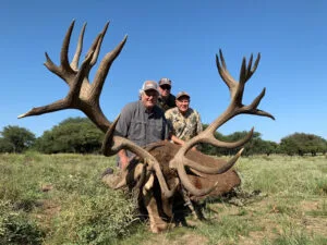 a group of men posing with a large antlers on a deer